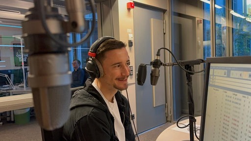 Werder-Kapitän Marco Friedl sitzt bei einem Studiobesuch bei Radio Bremen am Mikrofon.
