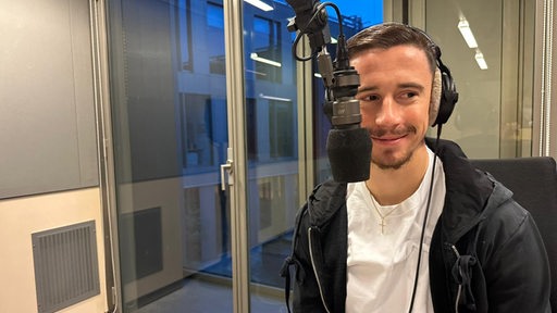 Werder-Kapitän Marco Friedl sitzt bei einem Studiobesuch bei Radio Bremen am Mikrofon.