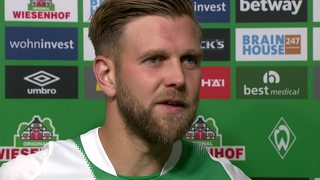 Werder-Stürmer Niclas Füllkrug vor einer Werbewand beim Interview.