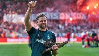 Werder-Stürmer Niclas Füllkrug reckt den Daumen hoch in Richtung der Fans und hält in der anderen Hand seine Torjägerkanone.
