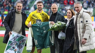 Niclas Füllkrug wird vor dem Spiel von Tarek Brauer, Klauls Filbry, Anne-Kathrin Laufmann und Frank Baumann verabschiedet. Dabei erhält er eine Jacke uund eine Bildercollage.