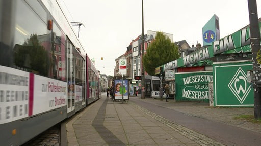 Blick auf die einfahrende Straßenbahn an einer Haltestelle im Bremer Viertel, an der an der Seite eine große Werder-Raute aufgemalt ist.