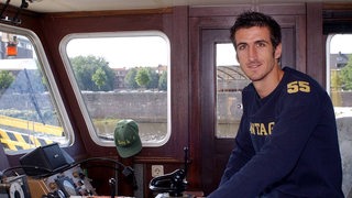 Johan Micoud sitzt als Kapitän auf einem Schiff. 