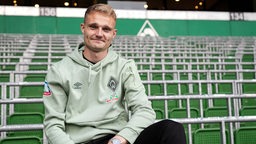 Werder-Neuzugang Amos Pieper sitzt lächelnd vor der Ostkurve im Weser-Stadion.