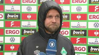 Werder-Stürmer Niclas Füllkrug mit deprimiertem Gesichtsausdruck und schwarzer Kapuze über dem Kopf beim Interview nach dem Pokalaus.