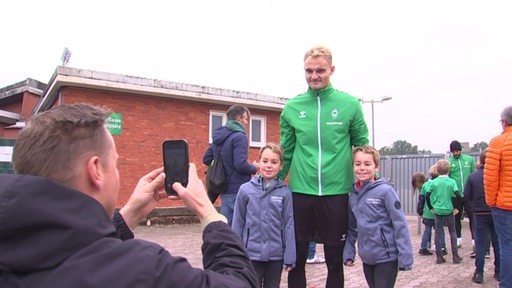 Der Werder Spieler Amos Pieper posiert mit zwei Jungen für ein Foto nach dem Training vor dem Weserstadion.