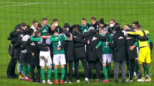 Das Team Werder Bremen steht in einem Huddle auf dem Spielfeld und steckt die Köpfe zusammen.