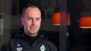 Werder-Trainer Ole Werner sitzt in seiner schwarzen Trainingsjacke bei einem Interview.