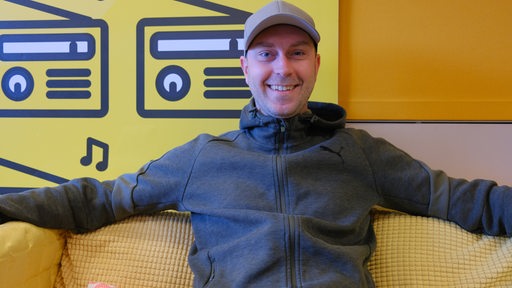 Werder-Trainer Ole Werner sitzt entspannt lächelnd auf dem gelben Sofa im Studio von Bremen Vier und wartet auf sein Interview.