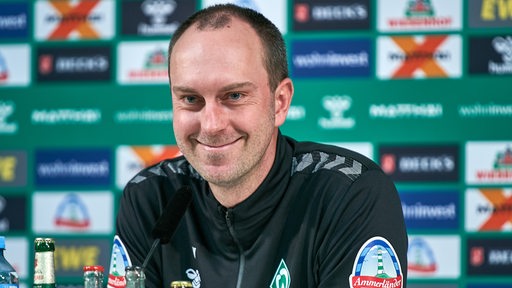 Werder-Trainer Ole Werner lächelt während einer Pressekonferenz.