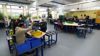 Mehrere Menschen sitzen an ihren Arbeitsplätzen in einer Werkstatt.