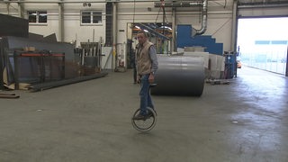 Der Mann Werner Bartsch, der auf einem Einrad in einer Werkstatt steht.