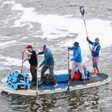 Vier Männer stehen im Fluss auf einem SUP und paddeln.