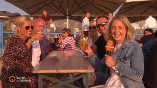 Reporterin Lea Reinhard sitzt auf einer Bank in der Sonne und interviewt Gäste des Weser-Strandbades in Bremerhaven.