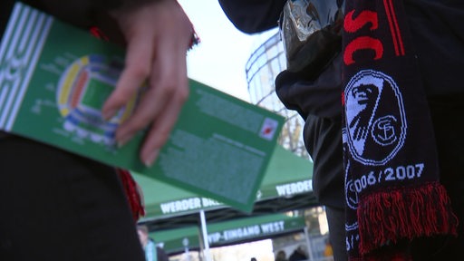 Fans des SC Freiburgs mit einer Eintrittskarte und einem Fanschal vor dem Weserstadion