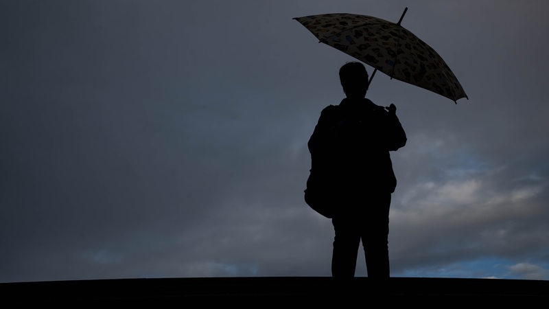Eine Frau steht mit einem Regenschirm auf einer Brücke. Am Himmel hängen dunkle Wolken.