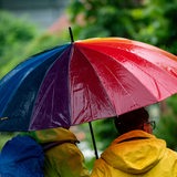 Spaziergänger sind bei Regenwetter mit einem bunten Regenschirm unterwegs.