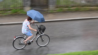 Ein Frau mit Schirm fährt auf dem Fahrrad durch den Regen.