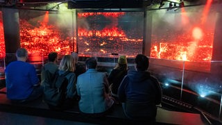Mehrere Personen sitzen im Dunkeln vor Leinwänden die Brände zeigen.