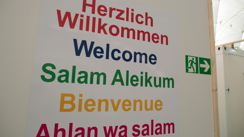 "Herzlich Willkommen" steht in verschiedenen Sprachen und Farben auf einem Schild.