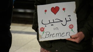 Eine Frau hält 2015 ein Wilkommensschild für Geflüchtete am Bremer Hauptbahnhof in der Hand