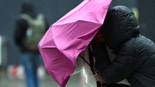 Passanten kämpfen mit dem Wind und ihrem Regenschirm. 