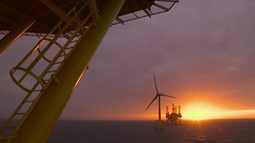 Eine Offshore Windkraftanlage und eine Ölbohrplattform vor dem Sonnenuntergang.