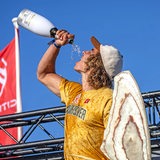 Lennart Neubauer, ein junger Mann, steht auf einem Podium und schüttet sich Champagner in den Mund.