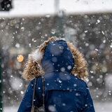 Eine Person mit Fellkaputze an der Winterjacke geht durch dichtes Schneegestöber.
