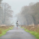 Ein Jogger läuft auf einem Feldweg bei nebligen Wetter.