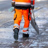 Ein Mitarbeiter vom Winterdienst geht mit einer Schneeschaufel über einen geräumten und gestreuten Fußweg.