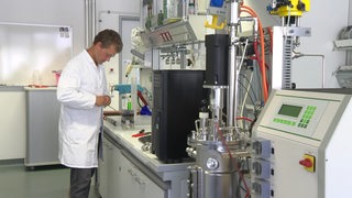 Ein Wissenschaftler steht in einem Labor mit einigen Gerätschaften und forscht zum Thema Wasserstoff.