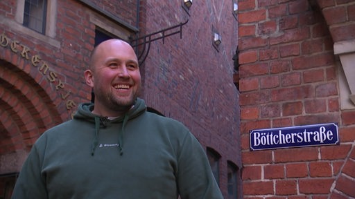 Daniel Schnadt mit dem Straßeschild der Böttcherstraße m Hintergrund 