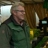 Ein Mann steht vor einem Tisch mit Gemüse und lacht.