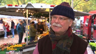 Ein Mann steht vor einem Stand auf einem Wochenmarkt.