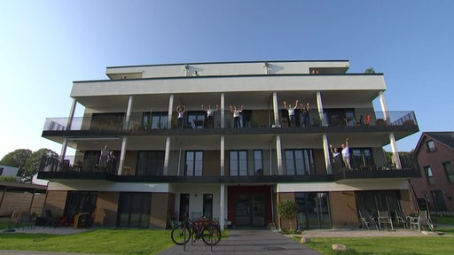 Eine Außenaufnahme vom Haus des Wohnprojekts Wolke 51 in der Überseestadt in Bremen. Auf den Balkonen stehen die Bewohner und winken zur Kamera.