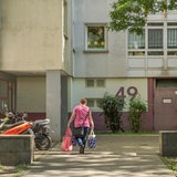 Eine Frau geht mit zwei Plastiktüten in den Eingang eines Sozialbaukomplexes