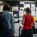 Zwei Studentinnen betrachten die Wohnungsanzeigen am Schwarzen Brett einer Universität