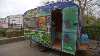 Ein mit Graffiti besprühter Wohnwagen, der zu einem begehbaren Kunstprojekt umgewandelt wurde, steht in einem Innenhof.