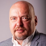 Ein Mann mit blauen Augen und Glatze schaut in die Kamera