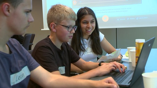 Drei Schüler:innen sitzen während eines Workshops gemeinsam vor einem Laptop.