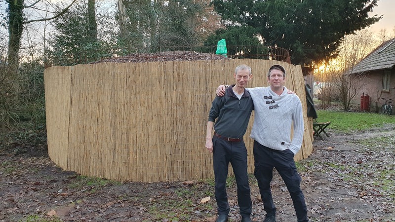 Die beiden Hofbewohner, Johannes Scholz und Stefan Zimmermann, stehen vor ihrem selbstgebauten Biomeiler "Hugo"