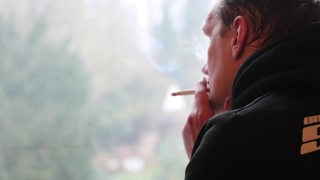 Ein Mann raucht eine Zigarette an einem Fenster