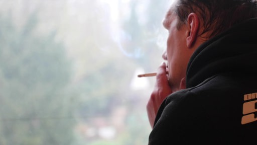 Ein Mann raucht eine Zigarette an einem Fenster