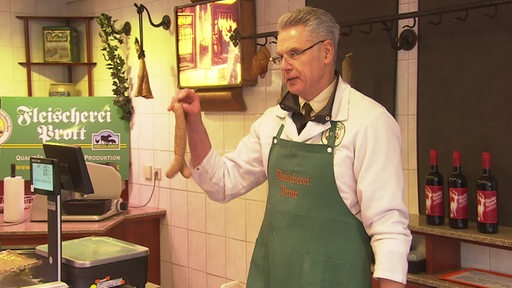 Der Fleischmeister Henning Prott steht mit Würstchen in der Hand in seiner Fleischerei.