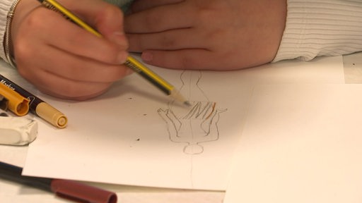 Eine Zeichnung von einer Model-Silhouette auf einem Blatt Papier wird per Hand mit Bleistift erweitert