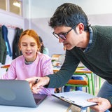 Ein Lehrer erklärt einer Schülerin etwas an ihrem Laptop.