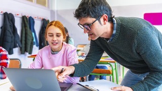 Ein Lehrer erklärt einer Schülerin etwas an ihrem Laptop.