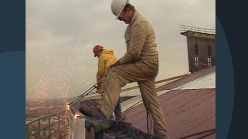 Zwei Arbeiter demontieren Teile des Gasspeichers.