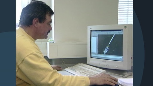 Ein Mann in einem gelben Pullover sitzt vor einem PC.
